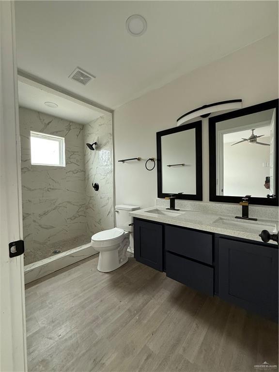 bathroom featuring ceiling fan, hardwood / wood-style floors, toilet, tiled shower, and vanity