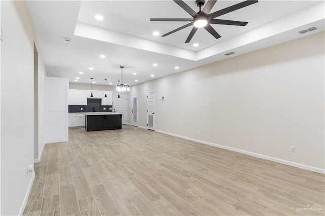 unfurnished living room featuring ceiling fan with notable chandelier and light hardwood / wood-style flooring