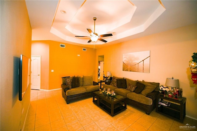 living room with a raised ceiling, ceiling fan, and light tile patterned floors