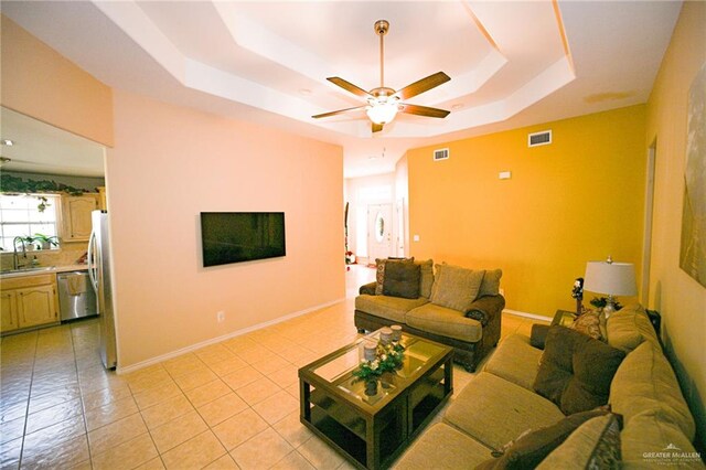 tiled living room with ceiling fan, a raised ceiling, and sink