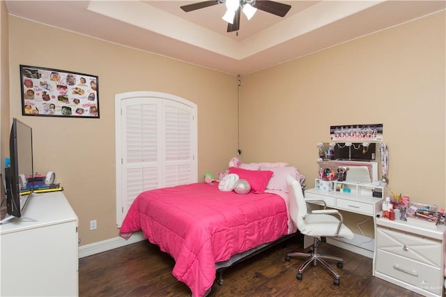 bedroom featuring ceiling fan, dark hardwood / wood-style flooring, and a tray ceiling