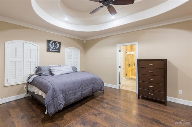 bedroom with crown molding, ensuite bath, a tray ceiling, dark hardwood / wood-style flooring, and ceiling fan