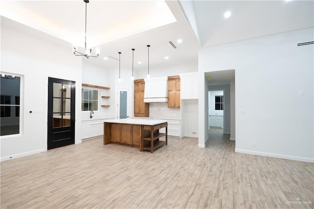 kitchen featuring a kitchen island, light hardwood / wood-style flooring, a towering ceiling, decorative light fixtures, and white cabinets