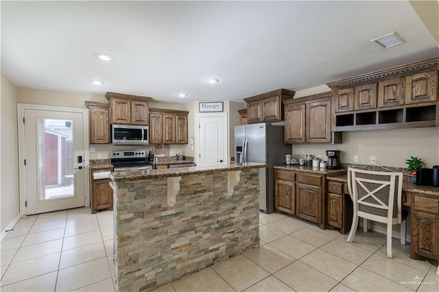 4517 Quail Ave, Mcallen, TX 78504 - kitchen featuring appliances with stainless steel finishes, light stone countertops, light tile patterned floors, a center island with sink, and a breakfast bar