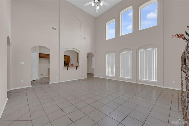 unfurnished living room with a towering ceiling, ceiling fan, light tile patterned flooring, baseboards, and arched walkways