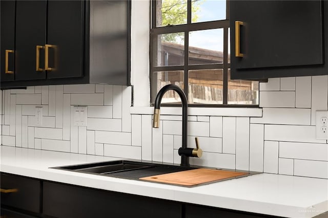 room details with a sink, decorative backsplash, light countertops, and dark cabinetry