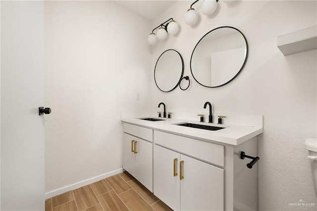 bathroom with double vanity, wood finish floors, a sink, and baseboards