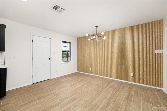 empty room with a notable chandelier, wood finish floors, wood walls, visible vents, and baseboards