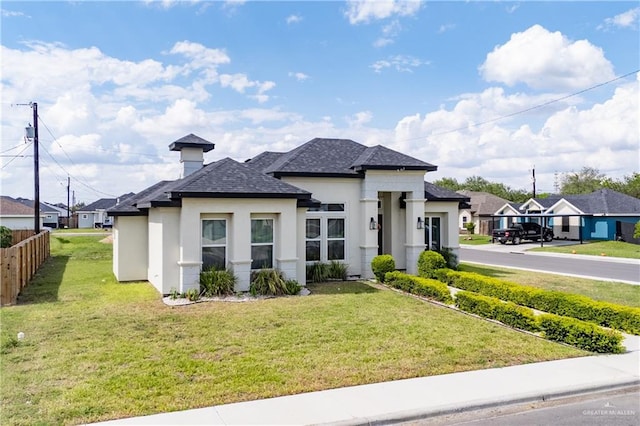 view of front of property featuring stucco siding, a shingled roof, a front lawn, and fence