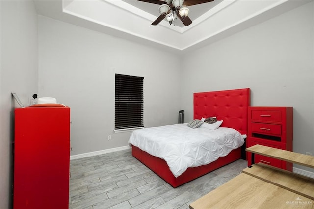 bedroom featuring a raised ceiling, ceiling fan, and light hardwood / wood-style flooring