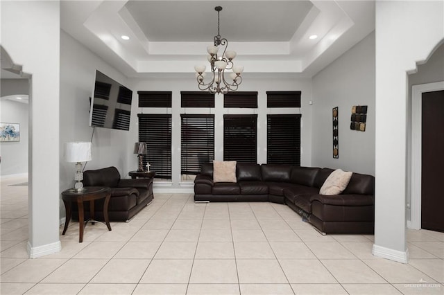 tiled living room featuring a raised ceiling and a chandelier