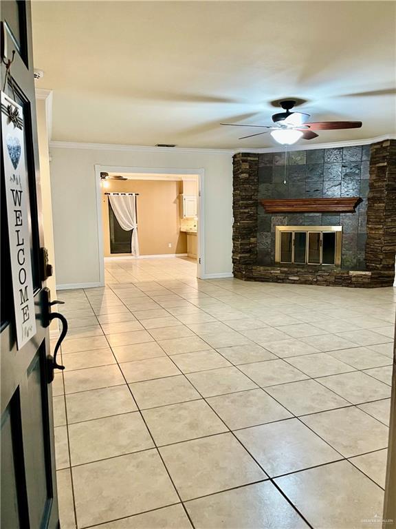 unfurnished living room with light tile patterned floors, ornamental molding, a stone fireplace, and ceiling fan