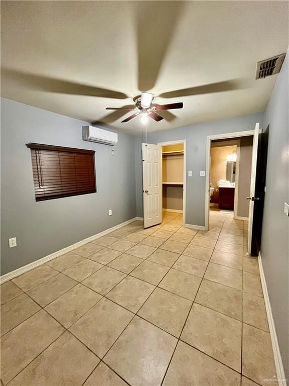 unfurnished bedroom with a spacious closet, a closet, a wall unit AC, ceiling fan, and light tile patterned floors