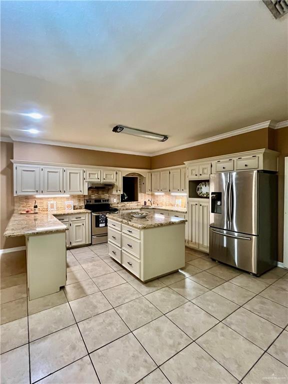 kitchen with light tile patterned floors, appliances with stainless steel finishes, a kitchen island, white cabinets, and light stone counters