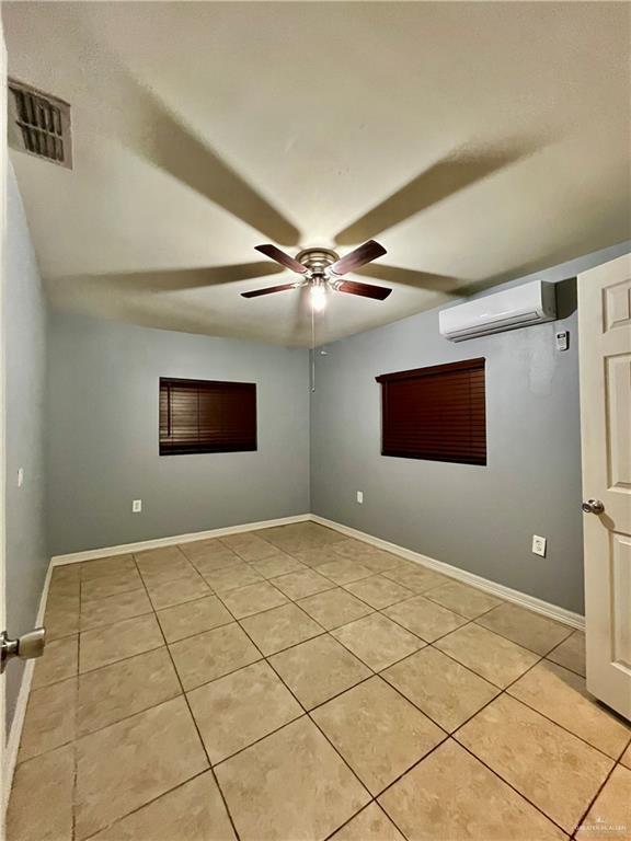 tiled empty room featuring ceiling fan and a wall mounted AC