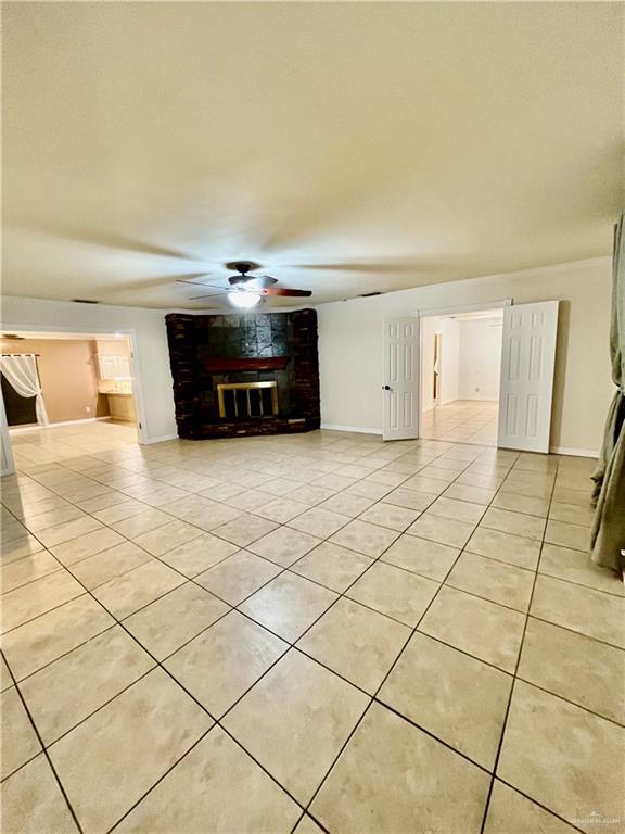 unfurnished living room featuring a brick fireplace, light tile patterned flooring, and ceiling fan