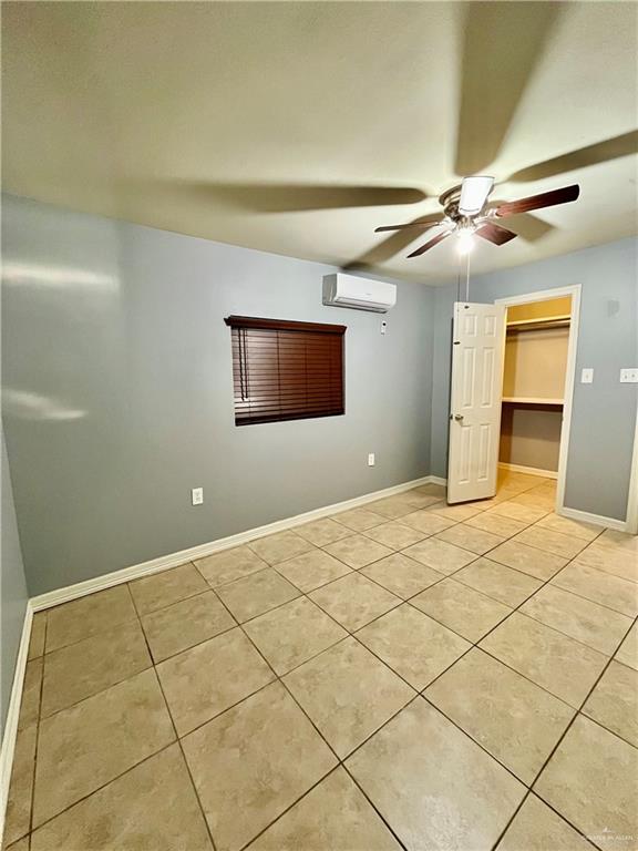 unfurnished bedroom with a spacious closet, a closet, a wall unit AC, ceiling fan, and light tile patterned floors