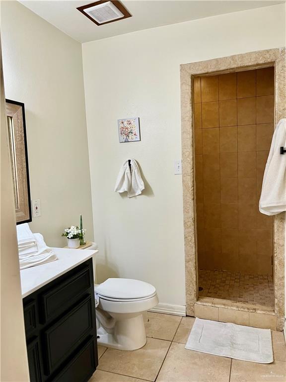 bathroom with toilet, vanity, tile patterned flooring, and a tile shower