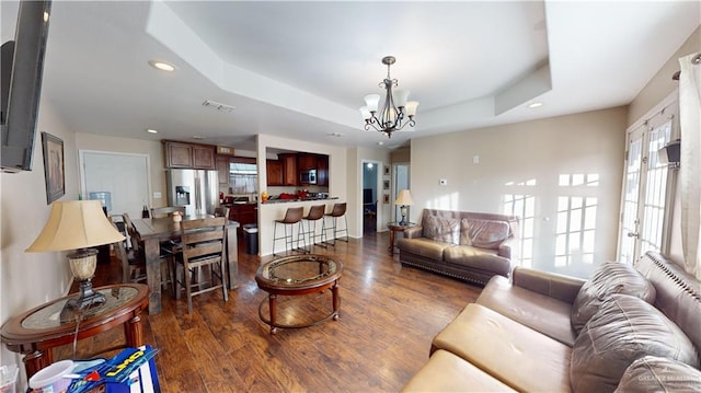 living room featuring a raised ceiling, dark hardwood / wood-style floors, and an inviting chandelier