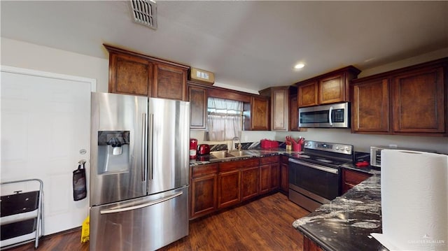 kitchen featuring appliances with stainless steel finishes, dark hardwood / wood-style floors, dark stone counters, and sink