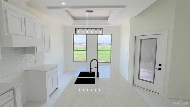 kitchen with decorative light fixtures, a raised ceiling, white cabinetry, and sink