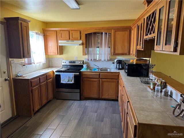 kitchen with electric range, tile counters, glass insert cabinets, under cabinet range hood, and a sink