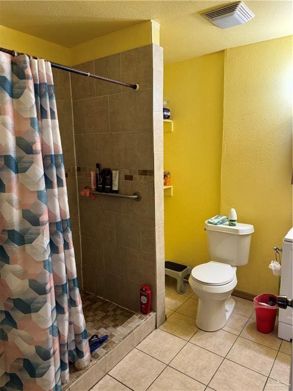 bathroom featuring toilet, visible vents, baseboards, a tile shower, and tile patterned floors