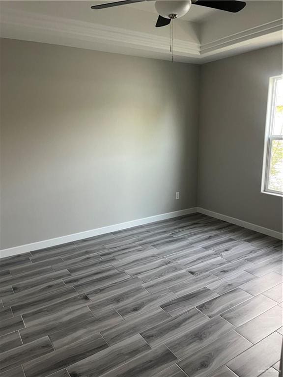 unfurnished room featuring a tray ceiling, dark wood finished floors, baseboards, and ceiling fan