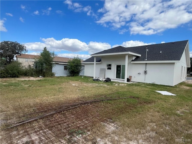 back of house featuring a yard, a shingled roof, and stucco siding