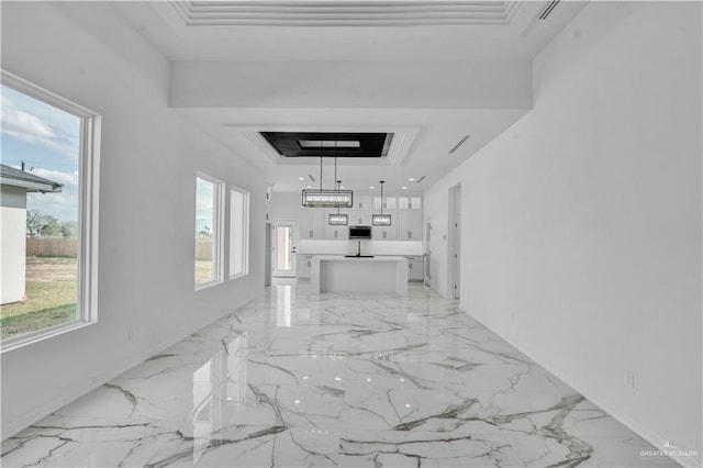 corridor with ornamental molding, a raised ceiling, plenty of natural light, and marble finish floor