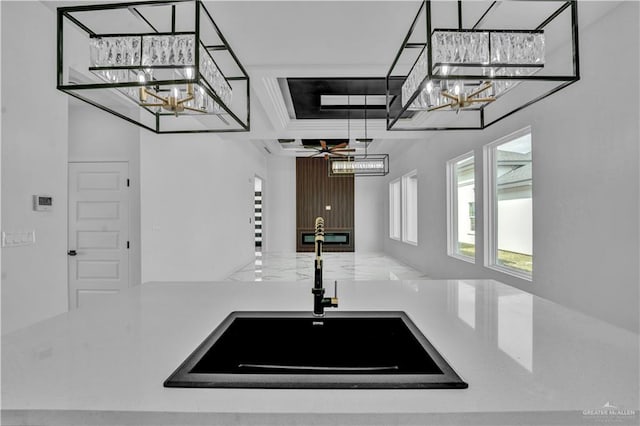 kitchen featuring hanging light fixtures, light countertops, crown molding, a sink, and ceiling fan with notable chandelier