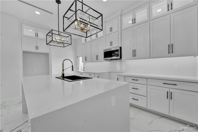 kitchen featuring white cabinets, stainless steel microwave, marble finish floor, an inviting chandelier, and a sink