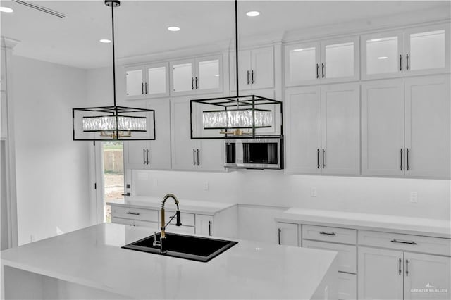 kitchen featuring stainless steel microwave, a sink, a center island with sink, and white cabinets