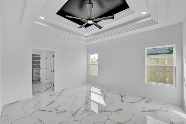 empty room with a tray ceiling, marble finish floor, crown molding, recessed lighting, and baseboards