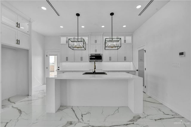 kitchen featuring white cabinetry, a kitchen island, stainless steel microwave, and a sink