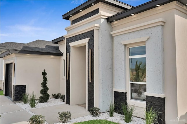 entrance to property with stone siding, roof with shingles, and stucco siding