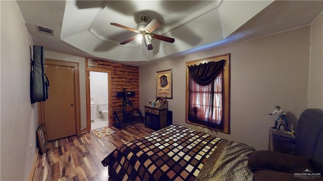 bedroom with connected bathroom, hardwood / wood-style flooring, a raised ceiling, and ceiling fan