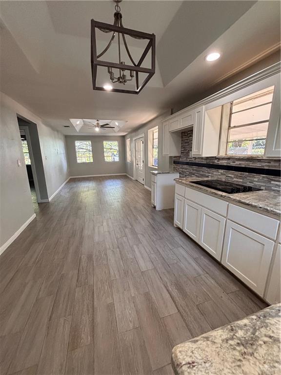 1012 S Inspiration Rd, Mission, TX 78573 - kitchen featuring open floor plan, white cabinets, baseboards, wood finished floors, and tasteful backsplash