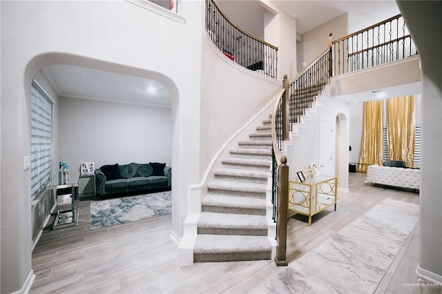 stairway featuring crown molding, a towering ceiling, and wood-type flooring