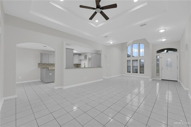 unfurnished living room with ceiling fan, light tile patterned floors, and a tray ceiling