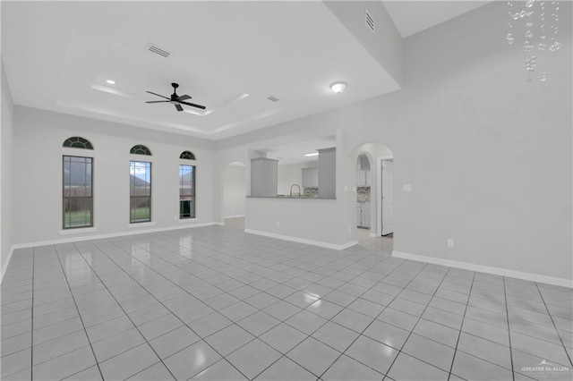 unfurnished living room with a raised ceiling, ceiling fan, and light tile patterned flooring