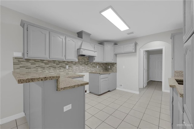 kitchen with kitchen peninsula, backsplash, light stone counters, extractor fan, and light tile patterned flooring