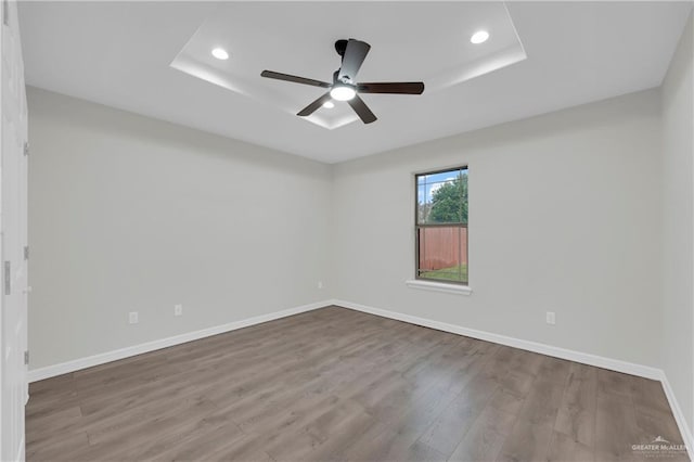 empty room with wood-type flooring, a raised ceiling, and ceiling fan