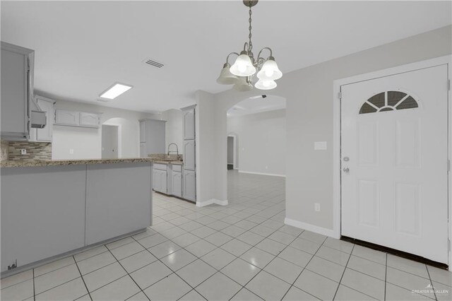 kitchen featuring light stone counters, sink, light tile patterned floors, and a chandelier