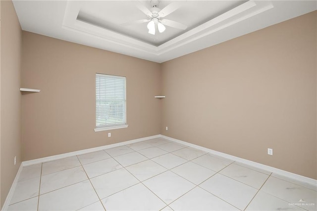 empty room featuring a ceiling fan, baseboards, light tile patterned floors, and a raised ceiling