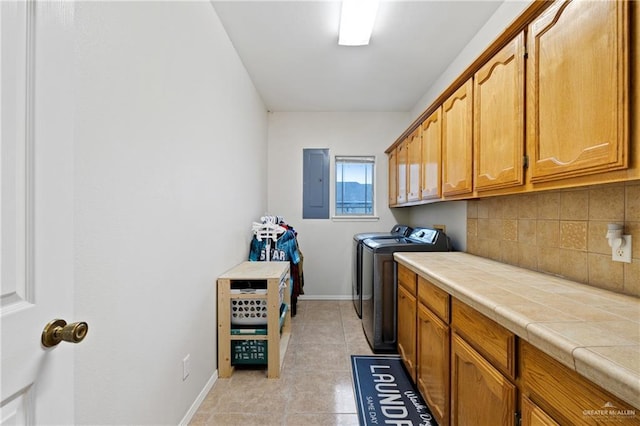 washroom with light tile patterned floors, washing machine and dryer, electric panel, and cabinets