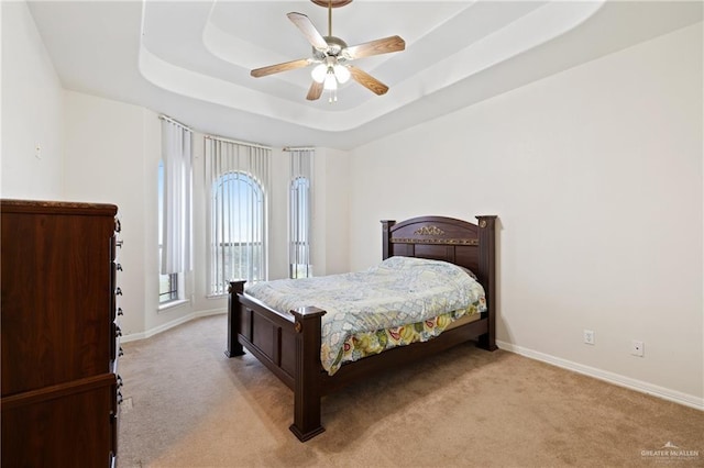 carpeted bedroom featuring ceiling fan and a tray ceiling