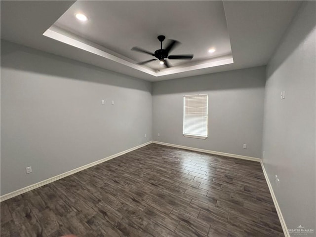 unfurnished room featuring a tray ceiling, ceiling fan, and dark wood-type flooring