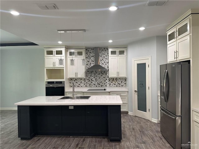 kitchen featuring sink, wall chimney exhaust hood, stainless steel appliances, dark hardwood / wood-style floors, and a center island with sink