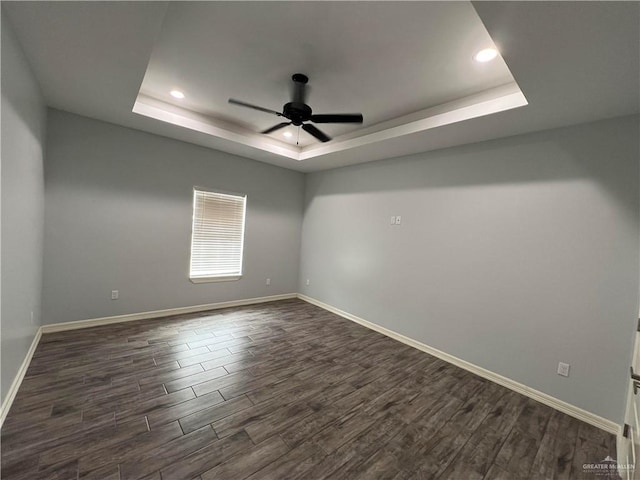 spare room with a tray ceiling, ceiling fan, and dark wood-type flooring